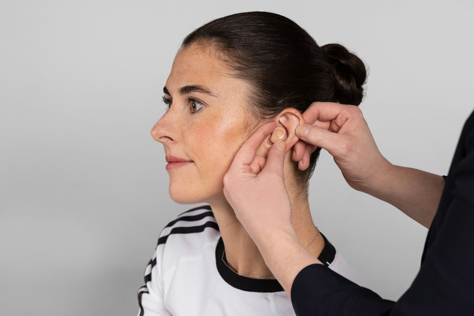 Fonoaudióloga colocando um aparelho auditivo intracanal na orelha de uma paciente. Foto de GN Group via Unsplash (https://unsplash.com/@gnhearingglobal).