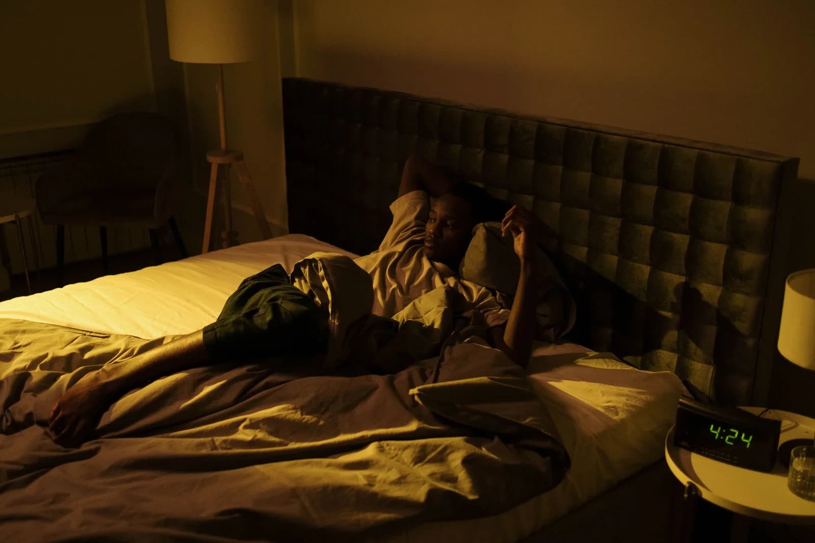 Homem deitado acordado na cama em quarto escuro, com dificuldade para dormir por causa do zumbido no ouvido. Foto de cottonbro studio via Pexels.