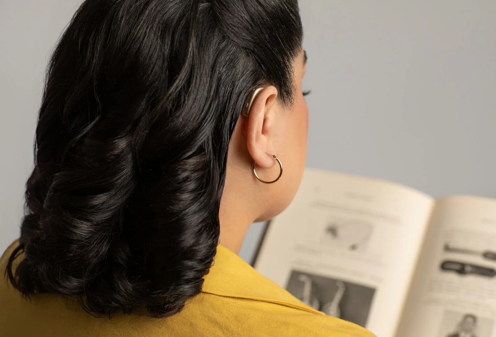 Mulher usando aparelho auditivo retroauricular atrás da orelha enquanto lê um livro. Foto de GN Group via Unsplash.