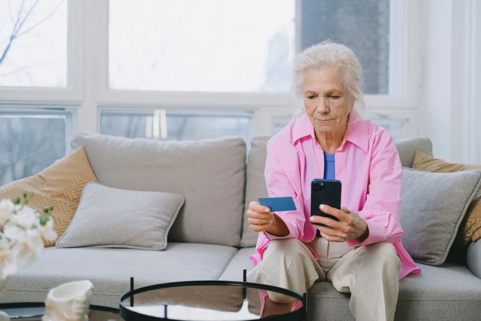Idosa usando o celular com o cartão na mão para comprar pela internet, ilustrando a compra de amplificador de som em marketplace. Foto de SHVETS production via Pexels.